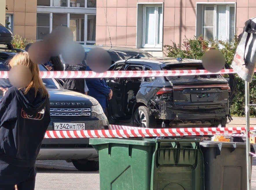 Пошкоджений чорний автомобіль на вулиці, поруч люди та розкидані уламки.