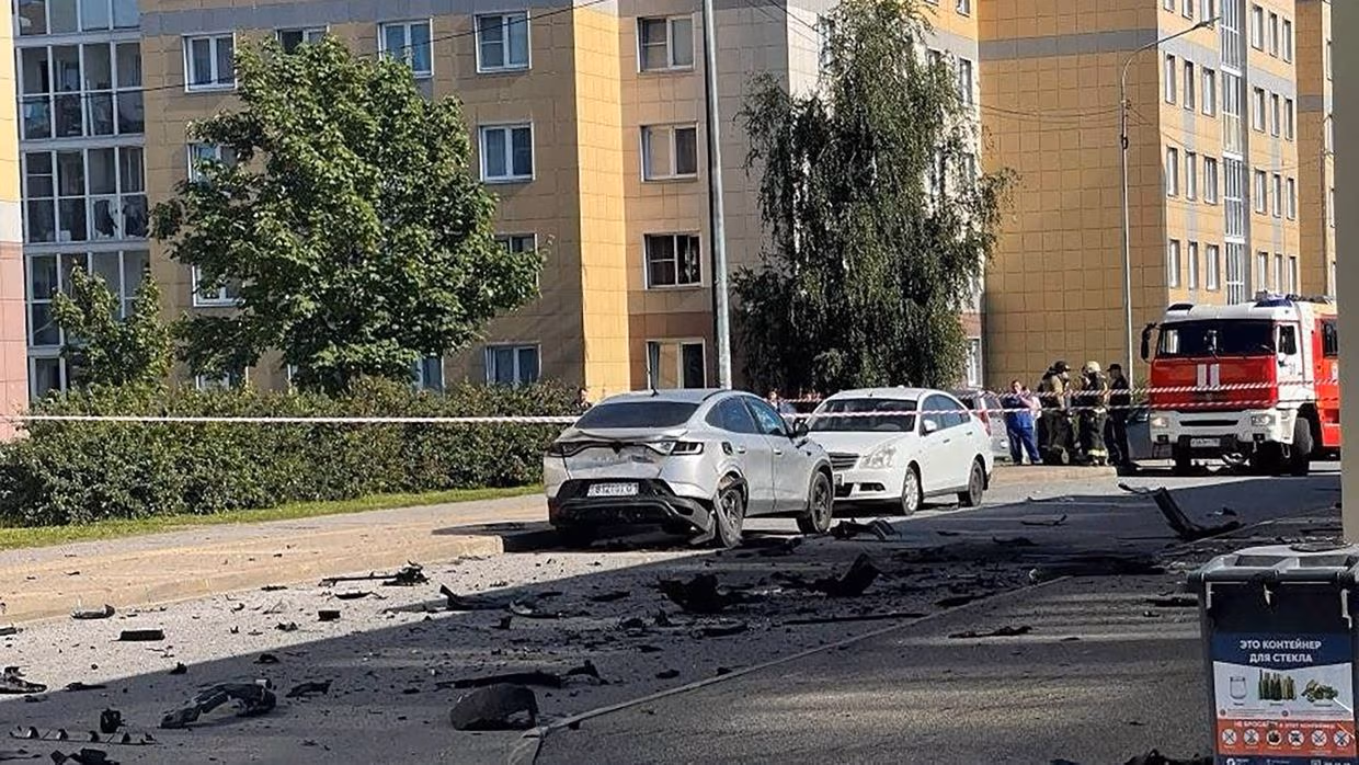 Дві машини біля житлового будинку, навколо уламки та працюють рятувальники.